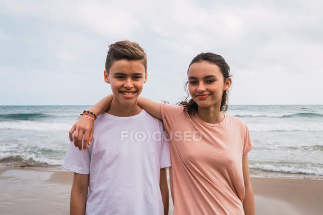 Retrato de la sonrisa adolescente chica y niño de pie en la playa - foto de stock