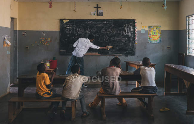 Камерун - Африка - 5 квітня 2018: Африканським дітям, сидячи в класі під час вчитель витираючи дошці — стокове фото