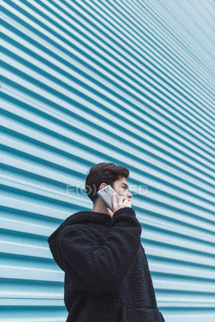 Молодий підліток стоїть на металевій стіні і розмовляє на смартфоні на вулиці — стокове фото