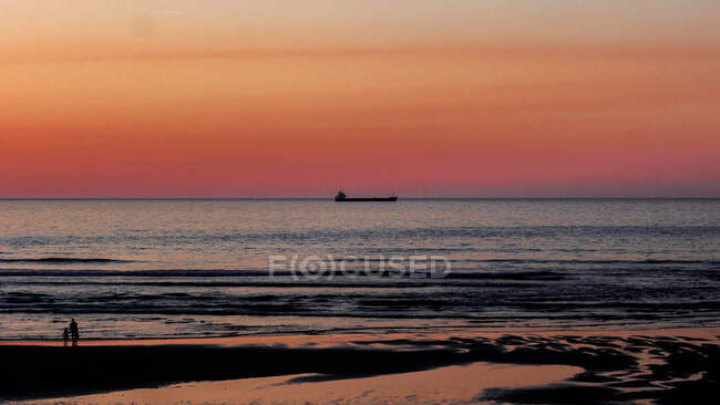 Vista brilhante das pessoas na costa à noite com céu colorido pôr do sol e veleiro longe no horizonte — Fotografia de Stock