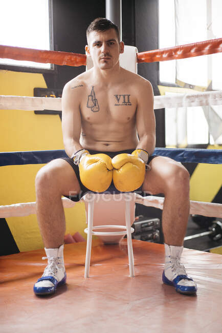 Hemdlos selbstbewusster Boxer in Handschuhen auf Hocker im Ring. — Stockfoto
