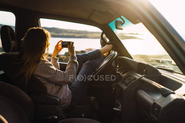 Donna scattare foto con smartphone in auto in natura — Foto stock