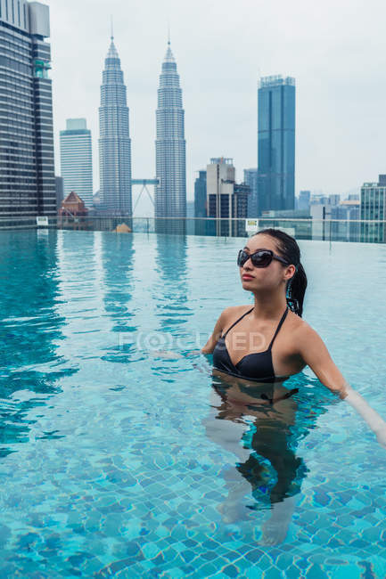 Азіатський жінка розслабляючий у басейні з хмарочоси на фоні — стокове фото