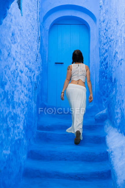 Rückansicht einer Frau, die auf einer blauen Treppe auf einer Straße in Marokko geht — Stockfoto