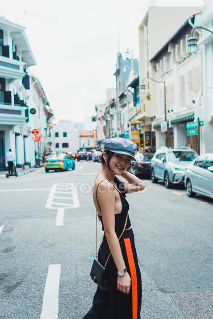 Sonriente joven asiática mujer caminando en la calle en la ciudad y mirando a la cámara - foto de stock