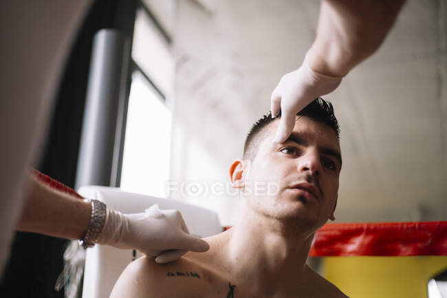 Mains de médecin méconnaissable vérifiant l'oeil du boxeur sur le ring de boxe. — Photo de stock