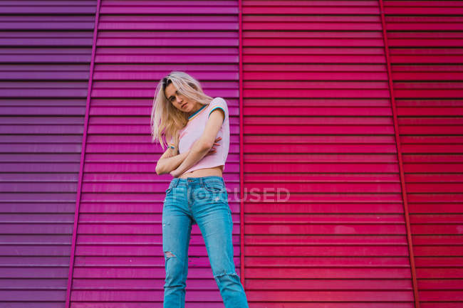 Fiduciosa donna bionda con le braccia incrociate in piedi contro una parete multicolore brillante — Foto stock