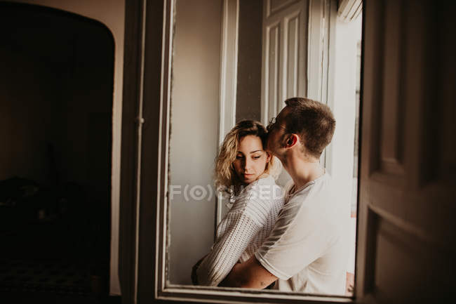 Casal romântico abraçando na janela em casa — Fotografia de Stock