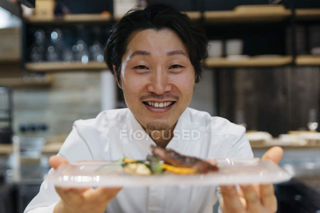 Усміхнений шеф-кухар показує тарілку їжі в ресторані — стокове фото