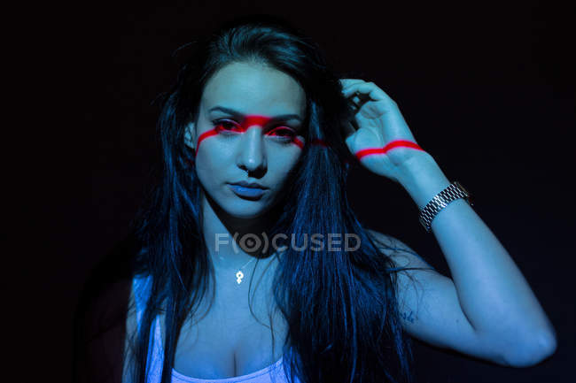 Jovem mulher atraente com linha vermelha no rosto e mão olhando para a câmera no fundo preto — Fotografia de Stock