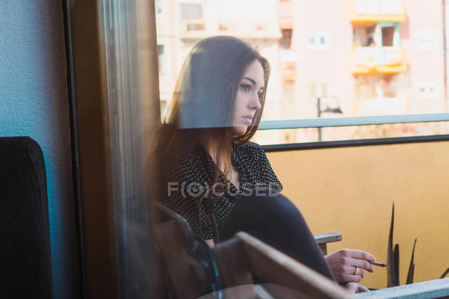 Nachdenkliche junge Frau sitzt auf Balkon und raucht — Stockfoto