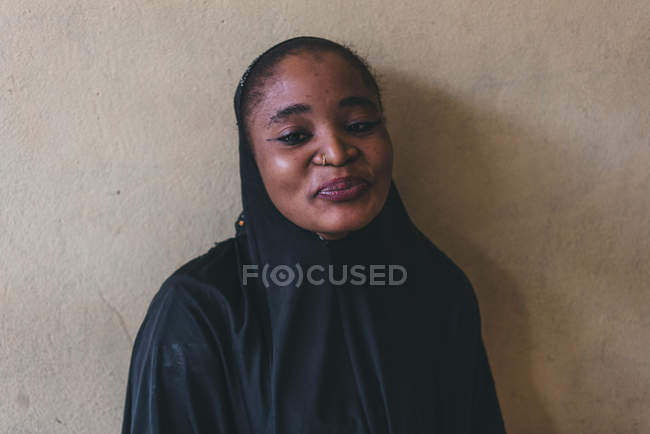 CAMARÕES - ÁFRICA - ABRIL 5, 2018: Mulher africana alegre com roupas pretas em pé na parede e olhando para a câmera — Fotografia de Stock