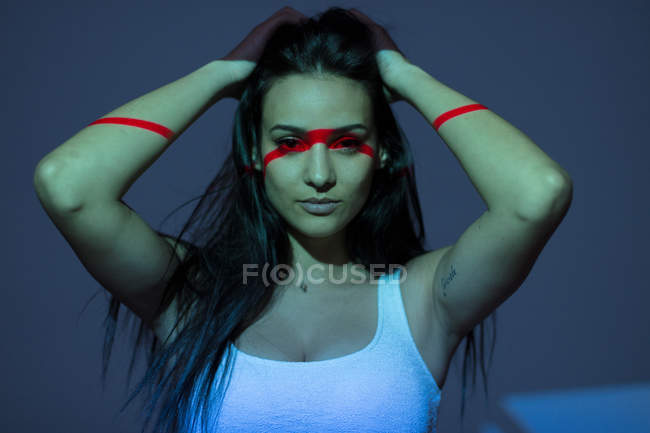 Молодая привлекательная женщина с красной линией на лице и руки на темном фоне — стоковое фото