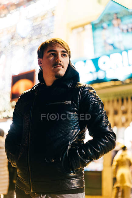 Thoughtful young man standing on illuminated street and looking away — Stock Photo