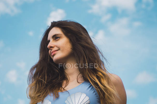 Cheerful woman in blue swimsuit standing against blue sky — Stock Photo