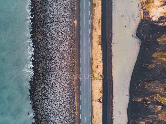 Сверху кадр узкой асфальтовой дороги, идущей вдоль каменного берега моря в Северной Исландии — стоковое фото