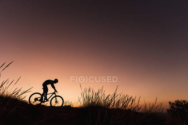 Вид сбоку на силуэт человека, едущего на велосипеде вниз по склону в закатных огнях. — стоковое фото