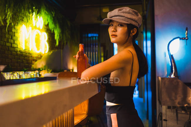 Élégante jeune femme asiatique assise dans un café et ayant une bouteille de boisson. — Photo de stock