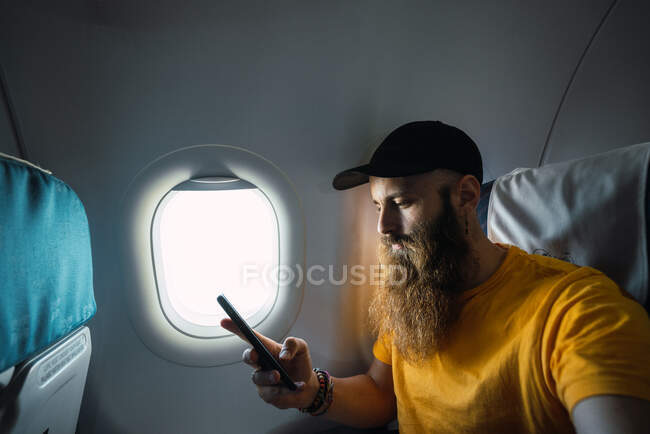 Бородатый мужчина со смартфоном внутри самолета — стоковое фото