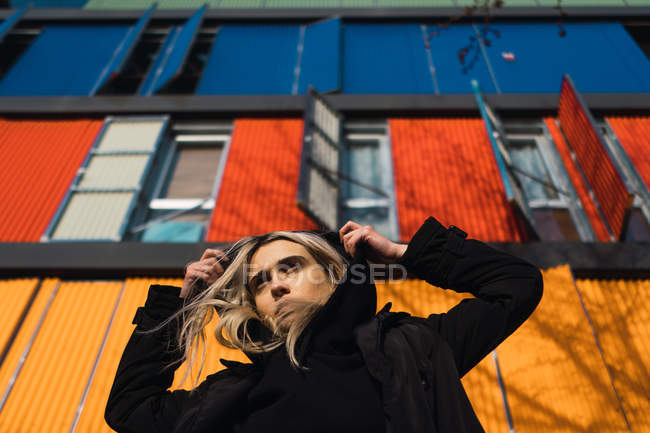 Attractive blonde woman looking away against colorful building — Stock Photo