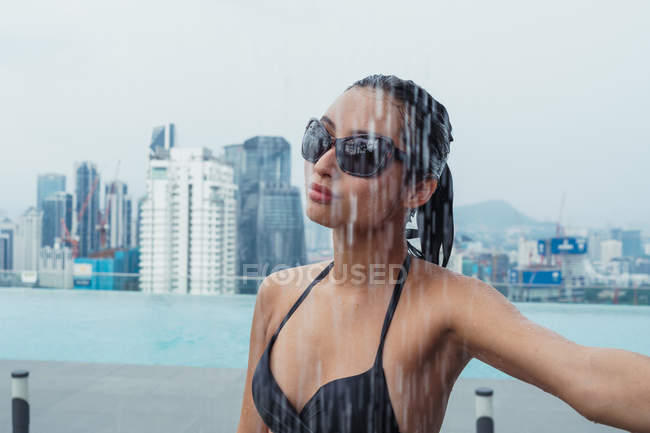 Pretty woman standing at pool shower with skyscrapers on background — Stock Photo