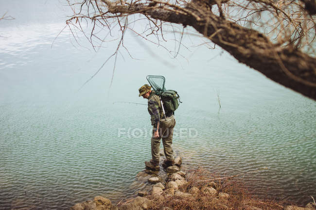 Fisherman standing with rod and balancing on rock at lake — Stock Photo