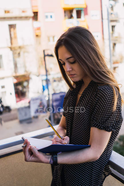 Giovane donna che scrive in blocco note sul balcone in città — Foto stock