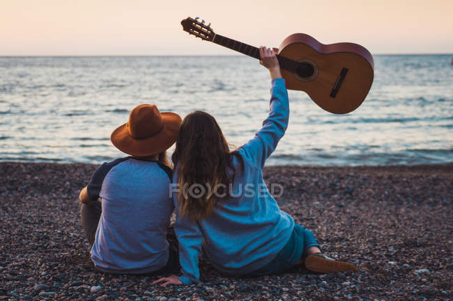 Homme et femme assis avec guitare sur la plage au bord de la mer — Photo de stock