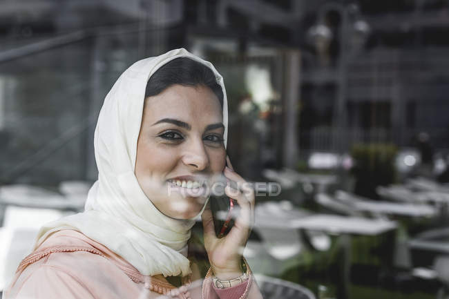 Femme marocaine avec hijab et robe arabe traditionnelle parlant au téléphone derrière le panneau de fenêtre — Photo de stock