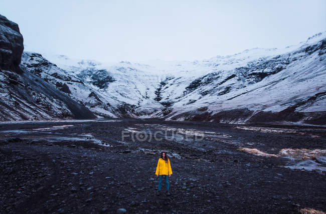 Mulher de casaco amarelo em pé perto de montanhas nevadas — Fotografia de Stock