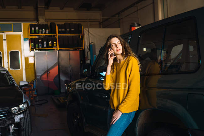 Frau telefoniert mit Smartphone, während sie sich in Garage an Auto lehnt — Stockfoto