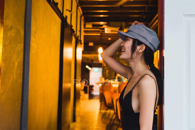 Laughing stylish Asian young woman leaning on wall at illuminated restaurant at night — Stock Photo