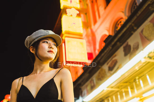 Молодая азиатка стоит ночью на освещенной улице и смотрит в сторону — стоковое фото