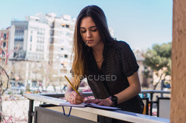 Молода жінка пише в блокноті на балконі в місті — стокове фото