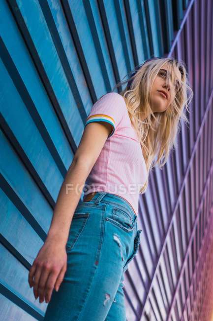 Mujer joven rubia apoyada en la pared azul en la calle - foto de stock