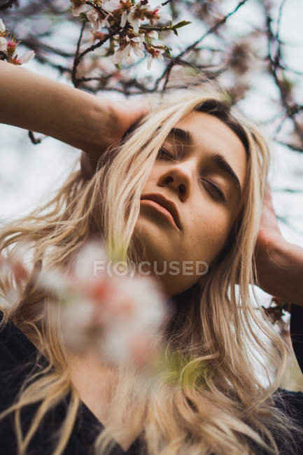 Junge blonde Frau in Blumen mit geschlossenen Augen und erhobenem Kopf — Stockfoto