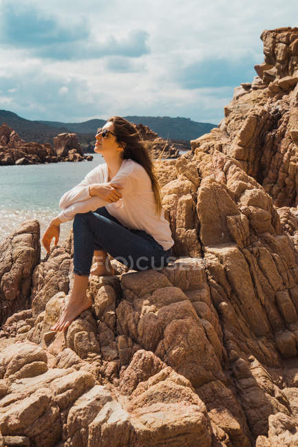 Женщина, сидящая на скалах у моря и смотрящая на вид — стоковое фото