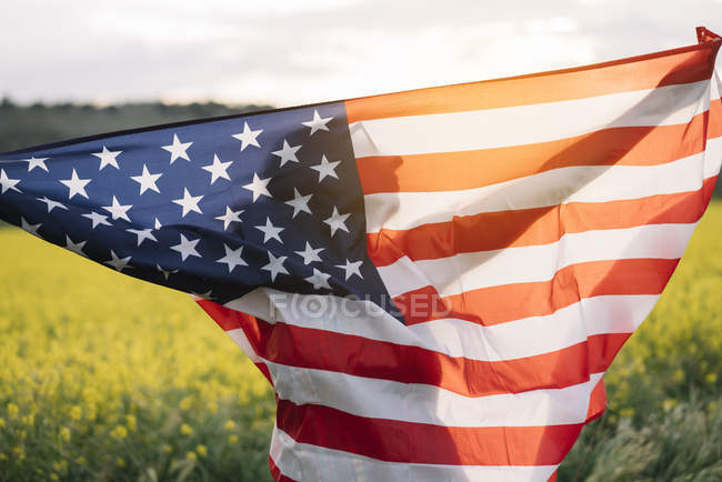 Mujer sosteniendo bandera americana en el campo con flores amarillas en el Día de la Independencia - foto de stock