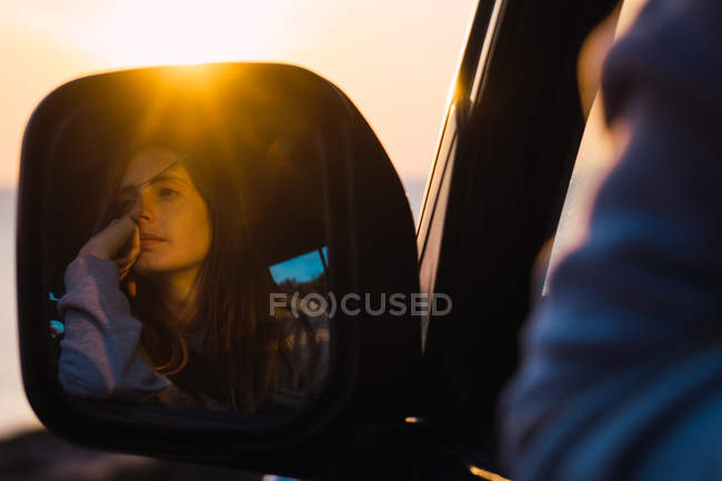 Reflet d'une touriste réfléchie assise en voiture au coucher du soleil — Photo de stock