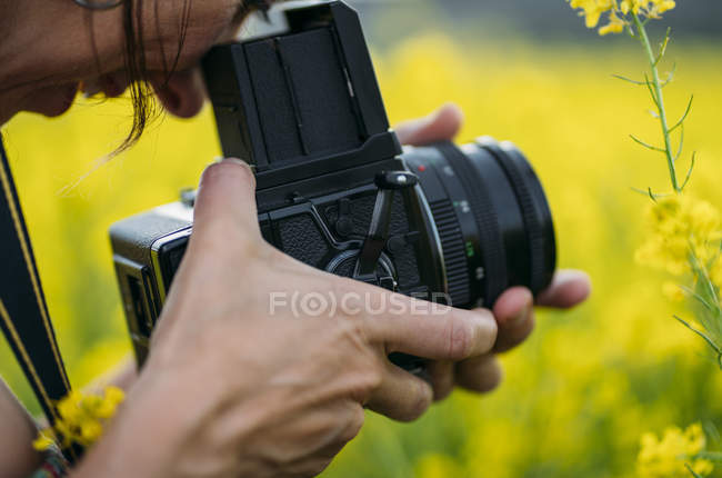 Close-up de mulher com câmera retro tirar foto na natureza com flores amarelas — Fotografia de Stock