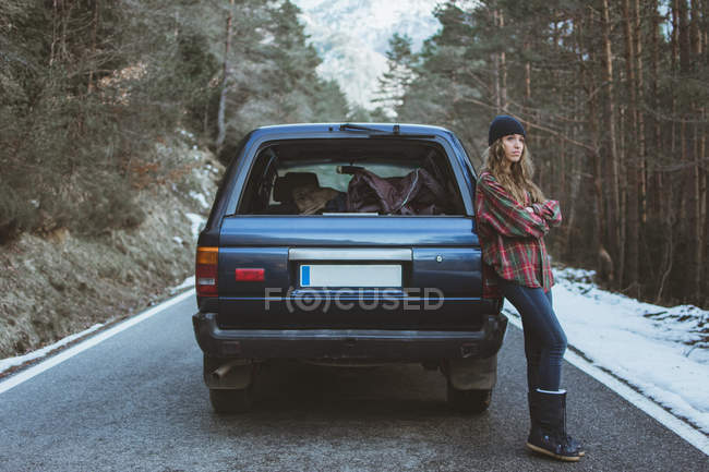 Woman leaning on car on road in mountains — Stock Photo