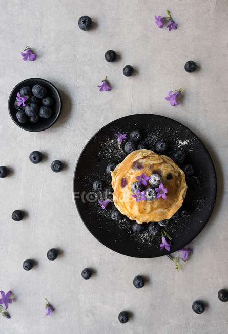 Montón de sabrosos bocadillos apetitosos con arándanos y flores púrpuras en el plato negro - foto de stock