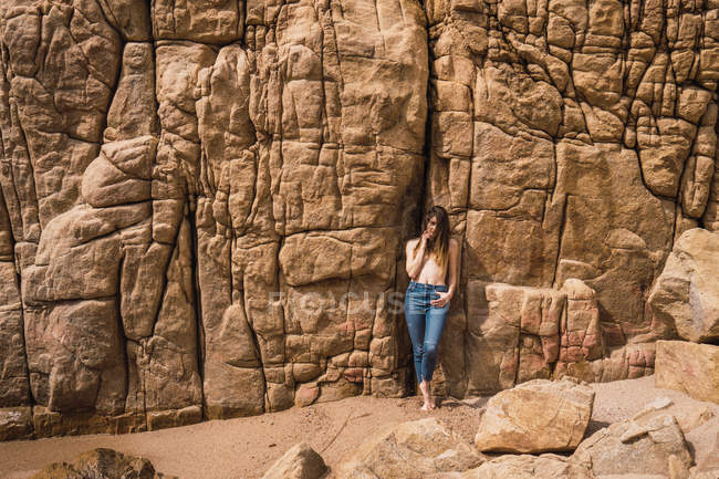 Topless attractive young woman in jeans standing and posing at rough rock — Stock Photo