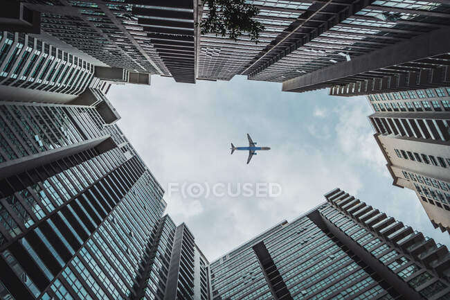 Знизу авіалайнер літає в хмарному небі над високими будинками в місті . — стокове фото