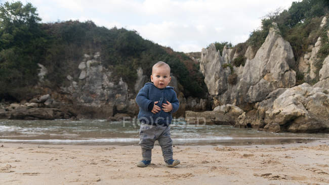 Portrait of toddler boy standing on lake shore with rocks — Stock Photo