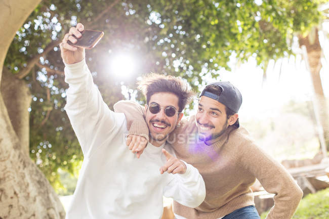 Glücklich lächelnde männliche Freunde machen Selfie mit Smartphone im sonnigen Park — Stockfoto