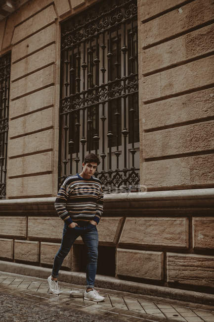 Молодий впевнений підліток в светрі, що йде по міській вулиці і дивиться на камеру — стокове фото