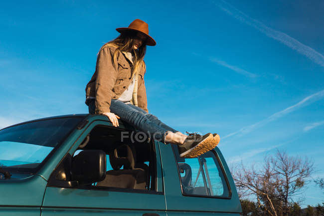 Mujer sentada en el techo del coche en la naturaleza bajo el cielo azul - foto de stock