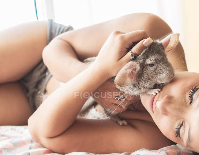 Jeune femme couchée au lit avec chinchilla — Photo de stock