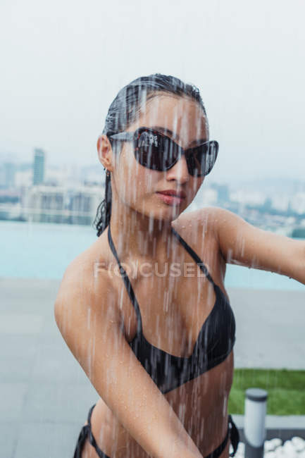 Pretty asian woman in sunglasses at pool shower in city — Stock Photo